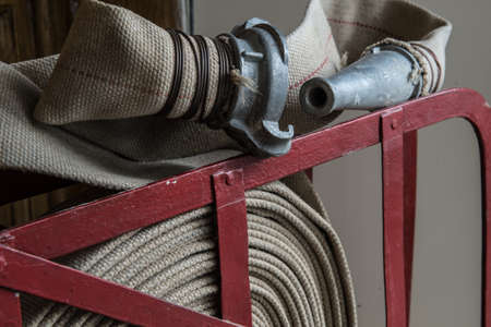 An old gray fire hose made of fireproof material attached to a special stand on a wooden wall. Connecting pipes made of metal.の写真素材