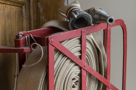 An old gray fire hose made of fireproof material attached to a special stand on a wooden wall....