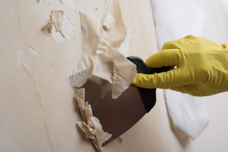 Preparing the wall for painting or sticking new wallpaper. Man in yellow gloves with a scraper in...