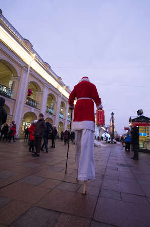 St. Petersburg, Russia - December 9, 2018: Santa Claus walks on stilts along Nevsky Prospect. Entertains passersby. In the hands of a suitcase. xmasのeditorial素材
