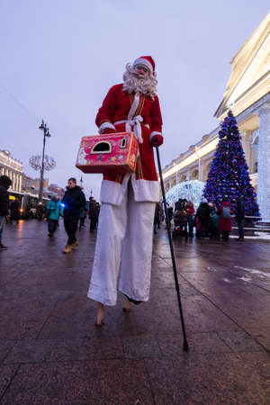 St. Petersburg, Russia - December 9, 2018: Santa Claus walks on stilts along Nevsky Prospect. Entertains passersby. In the hands of a suitcase. xmasのeditorial素材