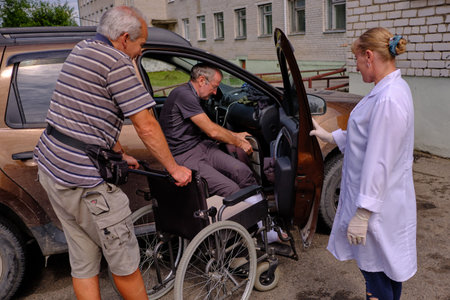 Belarus. Smarhon in the Grodno region - June 11, 2018: A man in a wheelchair at the emergency room of the city hospital. Broken leg plastered. Together assistant.のeditorial素材