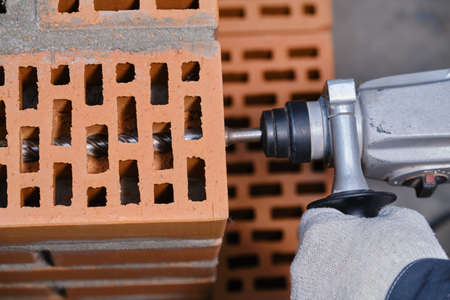 Stage of installation of a chemical anchor in a red building brick with cellular voids. Demonstration of the correctness of the actions of the builder. Close-up. Breaking a hole in a brick using a perforatorの写真素材