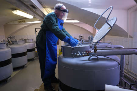 St. Petersburg, Russia - April 23, 2019: An employee of the scientific research institute in special uniforms protected from liquid nitrogen works in containers where rare plant seeds are stored.のeditorial素材