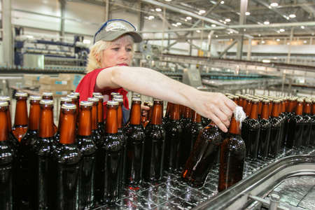St. Petersburg, Russia - June 21, 2006: Production line of the brewery. The conveyor controller selectively checks the quality of the dark beer bottles. Middle-aged womanのeditorial素材