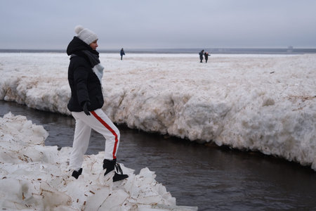 St. Petersburg, Russia - January 2, 2020: Tourists stroll along the coast of the Gulf of Finland. Sunny, fine day after a hurricane and an ice storm. Pieces of ice, open space, skyline. Russian crazy extremeのeditorial素材