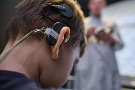 Hearing aid in the ear of a boy of 6-7 years old at a doctor's appointment. Auditory testing and selection of treatment methods using auditing equipment. Faces are unrecognizable.の写真素材