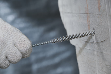Cleaning of small holes drilled in a concrete wall for chemical anchors from crumbs and dust. Work process. Hand in a glove. Metal brushの写真素材