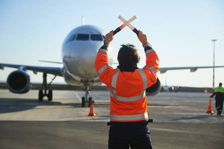 The runway traffic controller uses gestures and sticks to help the aircraft choose the correct trajectory around the airfield. Wearing a reflective vest