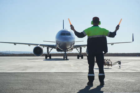 The runway traffic controller uses gestures and sticks to help the aircraft choose the correct trajectory around the airfield. Wearing a reflective vestの写真素材