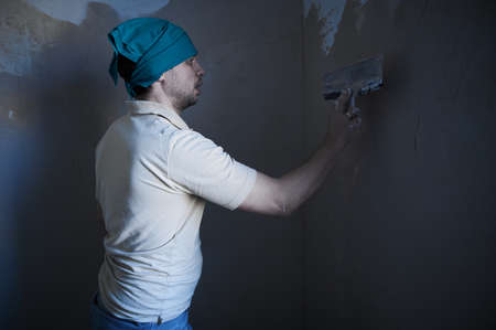 A 35-40 year old man during the process of plastering walls in an ordinary city apartment, makes repairs on his own, a portrait in a working environment, in a roomの写真素材