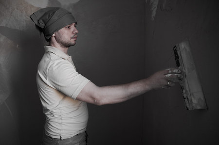 A 35-40 year old man during the process of plastering walls in an ordinary city apartment, makes...