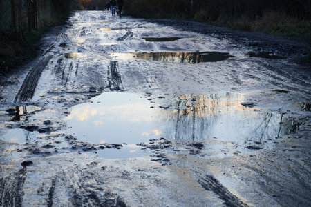 unrecognizable pedestrians walk cautiously along the broken dirt road. The coating is slippery, wet,...
