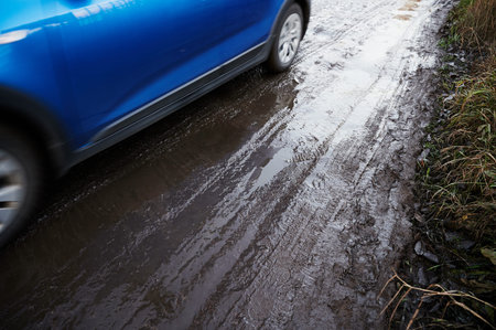 The blue car is driving through the mud. Left side of the vehicle, tire tracks behind liquid earthy...