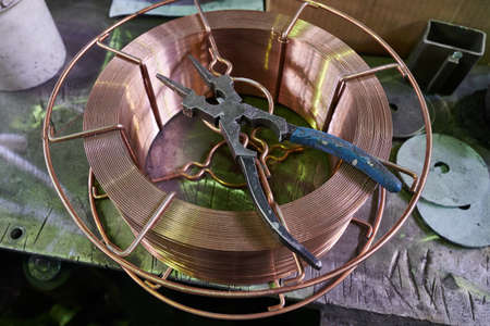 old working strong steel pliers for working on metal in the shop of the plant lie on a coil of copper wire of a large cross-section,の写真素材