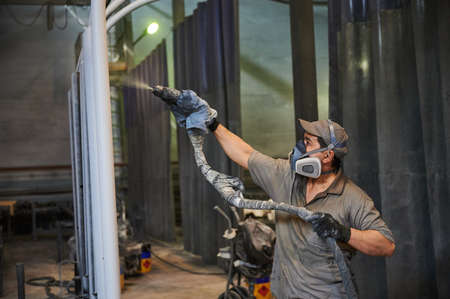 Young male painter with a spray gun paints the lamp posts at a metalware factory, wearing a protective maskのeditorial素材