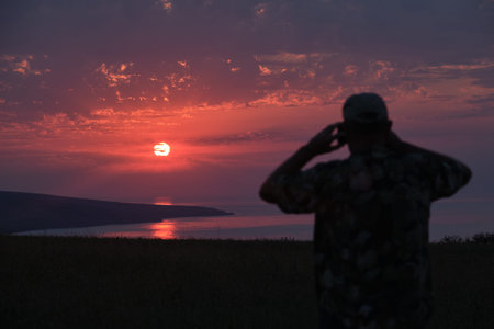 blurred silhouette of an unrecognizable man from the back who photographs a beautiful pink summer...