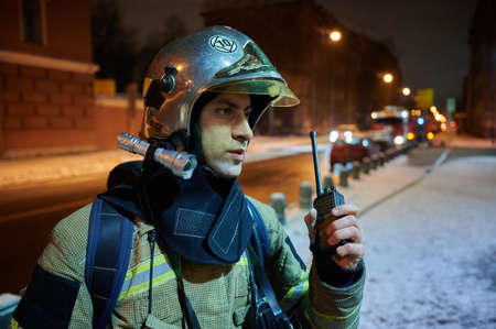 A firefighter in full gear, wearing a helmet with a protective glass visor, during a firefighting exercise at nightのeditorial素材