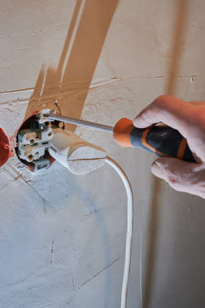 Dangerous connection of an electrical plug to a new socket without a decorative cover installed on a freshly plastered wall.の写真素材