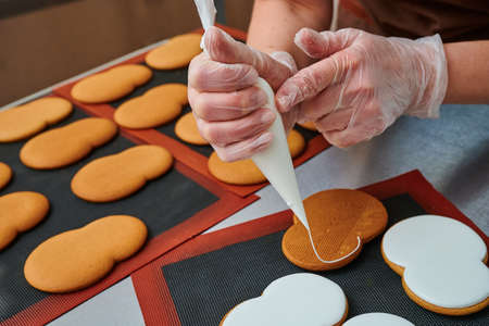 applying a layer of glaze to a confectionery product using a pastry bag. A row of gingerbread cookies on the kitchen table. Confectioners inventory. Product surface decorationの写真素材