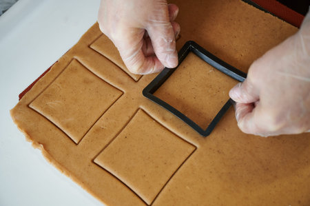 The confectioner forms gingerbread cookies using an original rectangular cutting. Womans hands in...