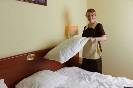 Young blonde woman 39 years old in the uniform of a hotel maid. Next to a large double bed. Change bed linen and beddingの写真素材