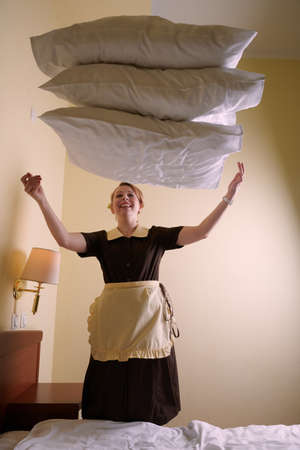 Young blonde woman 39 years old in the uniform of a hotel maid. Next to a large double bed. Change bed linen and beddingの写真素材