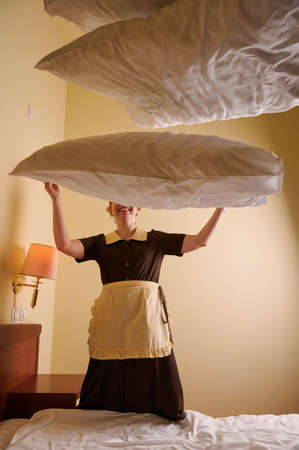 Young blonde woman 39 years old in the uniform of a hotel maid. Next to a large double bed. Change bed linen and beddingの写真素材