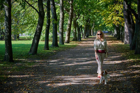 young blonde woman in light casual clothes walks with a Cavalier King Charles Spaniel dog in the historical center of the small town of Kronstadt on a sunny fine day along the cobblestonesの写真素材