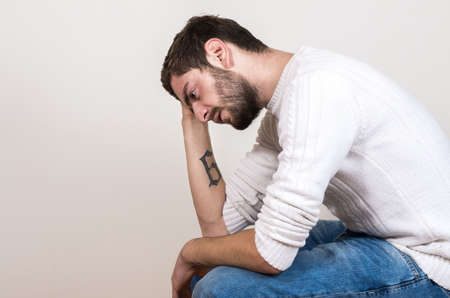 sad handsome man with beard sitting on chairの写真素材