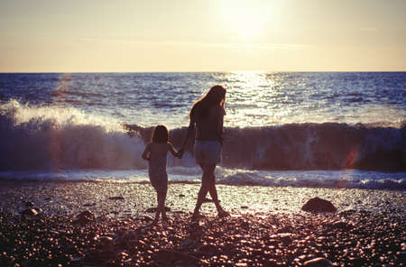 Mother with child girl at the sea beach on sunsetの写真素材