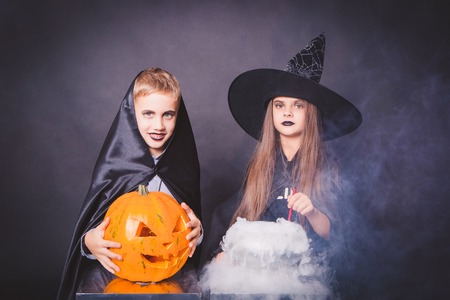 funny girl with a boy in a witch costume for Halloween with pumpkin Jack on a dark background with smokeの写真素材