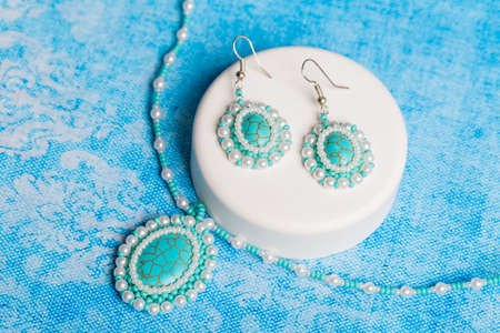 Earrings and a pearl necklace with a white box are on the table with a blue background. Close upの写真素材