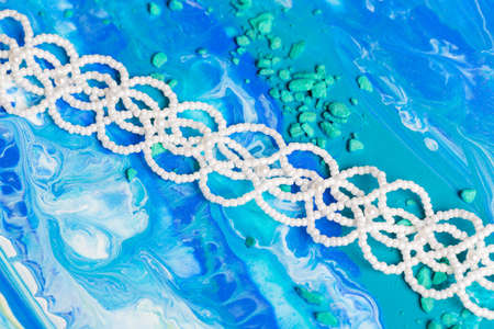 Handmade bracelet made of white beads on canvas with blue colors. Close upの写真素材
