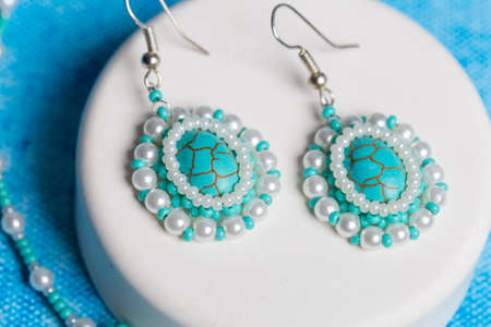 Earrings and a pearl necklace with a white box are on the table with a blue background. Close upの写真素材