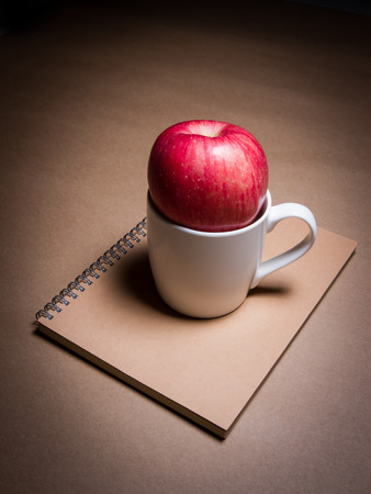 an apple and a cup on a brown notebookの写真素材