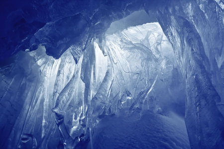 blue ice cave covered with snow and flooded with lightの写真素材