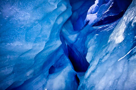 blue ice cave covered with snow and flooded with lightの写真素材