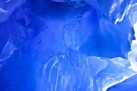 blue ice cave covered with snow and flooded with lightの写真素材
