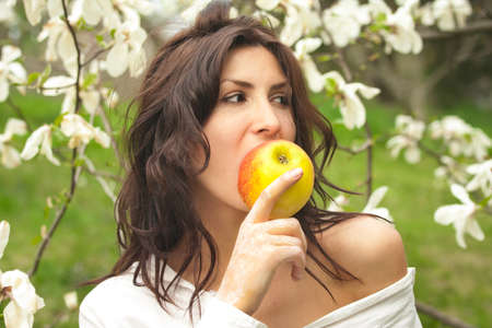 Beautiful young girl eating an apple in the parkの写真素材