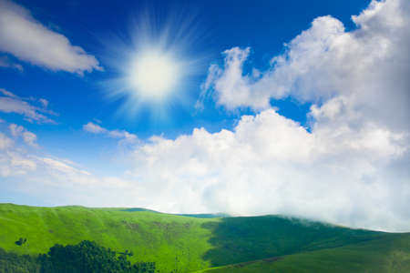 Blue cloudy sky and green spring hillの写真素材