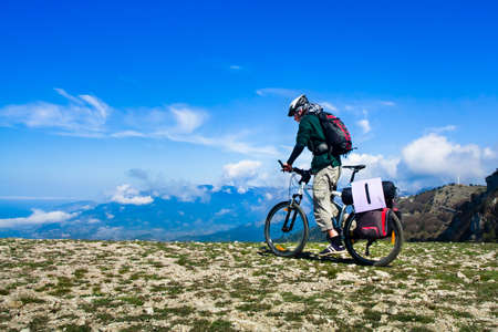 Young man riding a bike over the precipice in the mountainsの写真素材