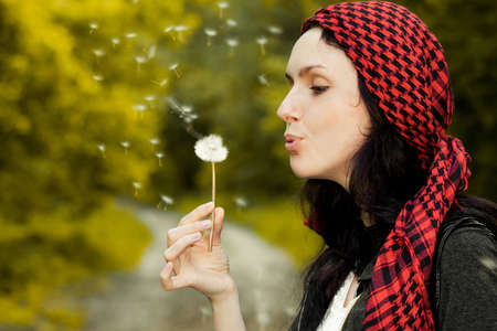 Girl blowing on white dandelion in the forestの写真素材