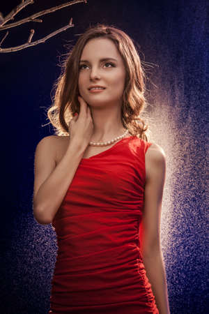 Beautiful girl in a red dress, standing behind the falling waterの写真素材