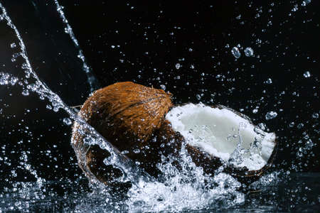 cracked coconut with big splash on black backgroundの写真素材