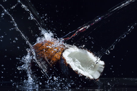 cracked coconut with big splash on black background