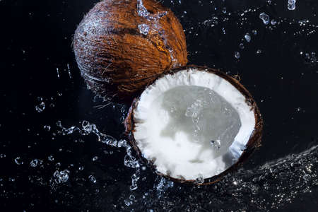 cracked coconut with big splash on black backgroundの写真素材