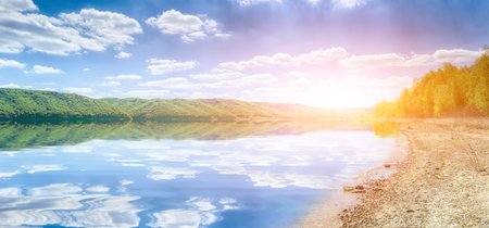 Coast of the big river under sunshine. Beautiful river banks with green trees and bushesの写真素材