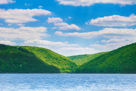 green hills on the bank of the river. River landscape and beautiful blue sky with white cloudsの写真素材