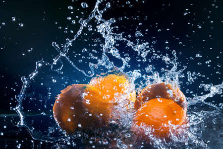 ripe oranges lying on the mirror in a spray of water on dark backgroundの写真素材